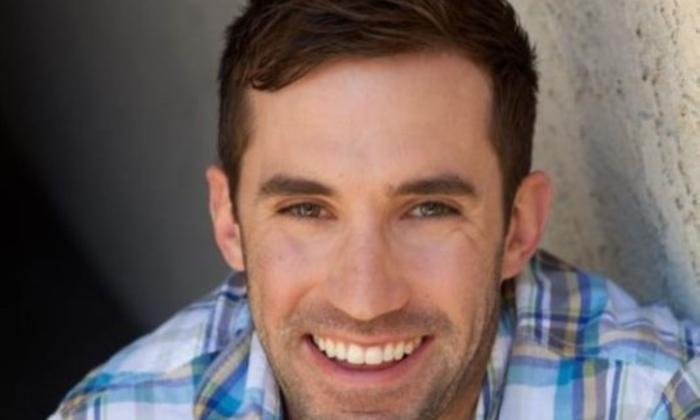 Michael Palascak wears a plaid shirt and poses in front of a white and black backdrop.