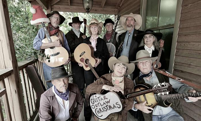 Nine musicians on a cabin porch, in clothing of the Old West