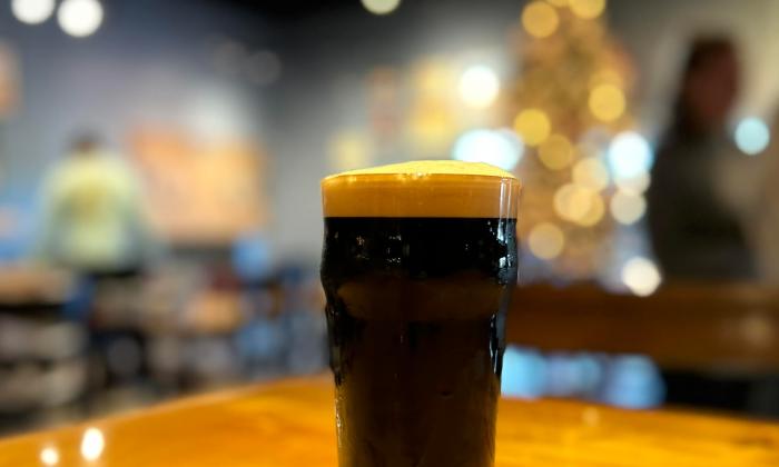 A glass of dark beer on a wooden bar, with a soft-focused Christmas tree in the background