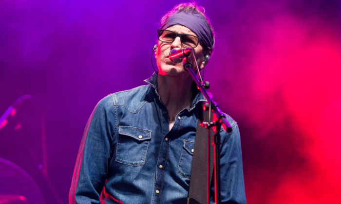 The lead vocalist for BoDeans performs on stage in front of a purple and pink backdrop.