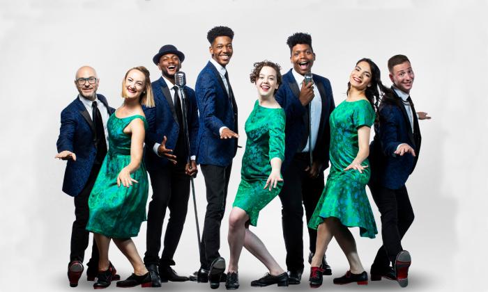 Eight dancers in tap shoes on a white stage