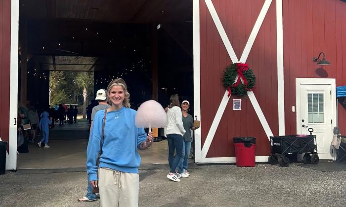 A teenager with a serving of cotton candy outside a red barn