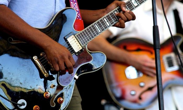 Two men playing guitars on stage, focused on the guitars and their hands