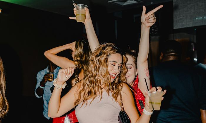 Two young women smile and dance at a party. 