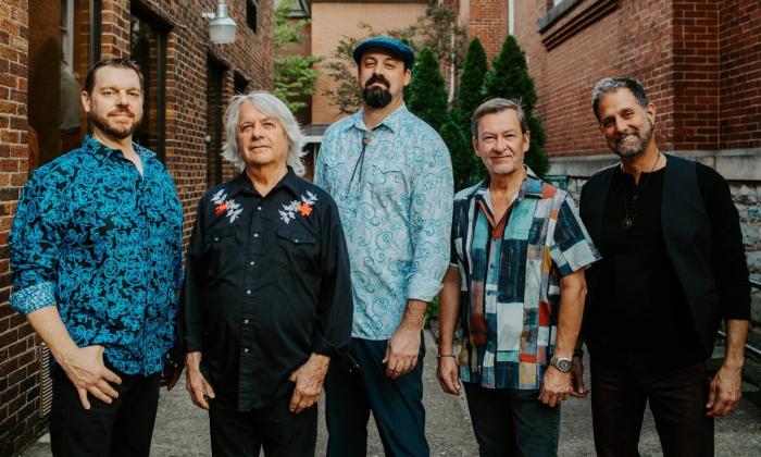Bandmates from Pure Prairie League smile and pose in front of two brick buildings.