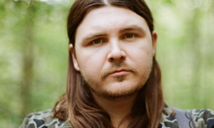 Ben Chapman stands before a softly blurred backdrop of clustered trees.