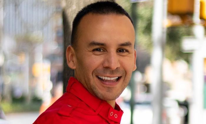Pedro Gonzalez wears a red shirt and smiles in front of a blurred backdrop.