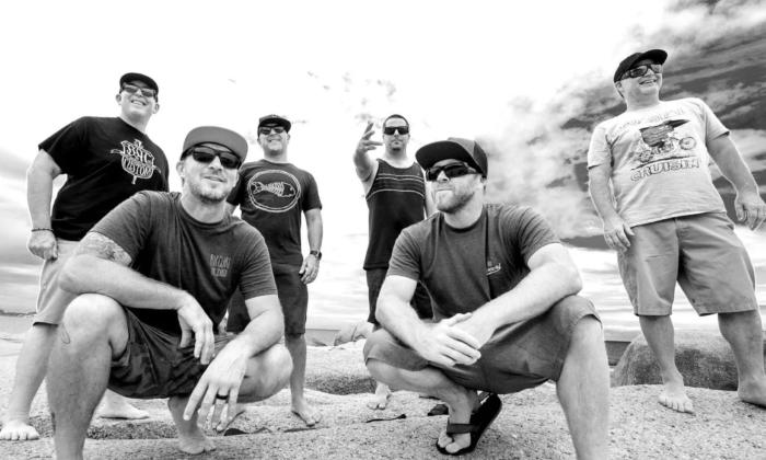 Bandmates from Slightly Stoopid pose on rocks in front of an ocean.