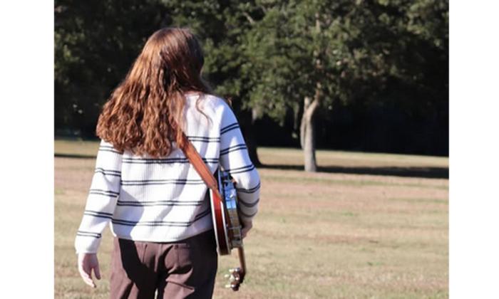 Paige Bechtold walking away from camera, with her banjo.