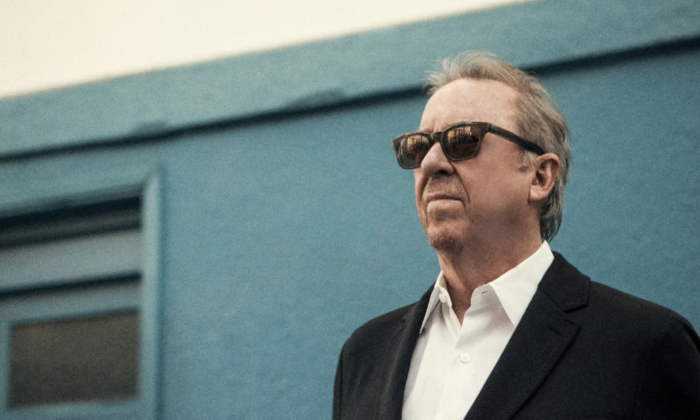 Boz Scaggs wears black glasses and poses in front of a grey backdrop.
