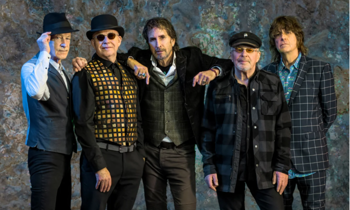 Bandmates from the Fixx wear dark clothing and pose in front of a textured backdrop.