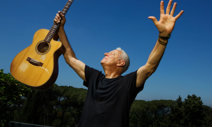 Tommy Emmanuel shuts his eyes and holds his guitar in the air.