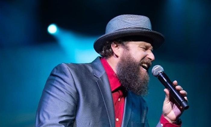John Nemeth performs on stage in a blue blazer and a matching cap.