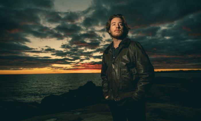 Quinn Sullivan, dressed in dark clothing, poses before a backdrop of a setting sun.