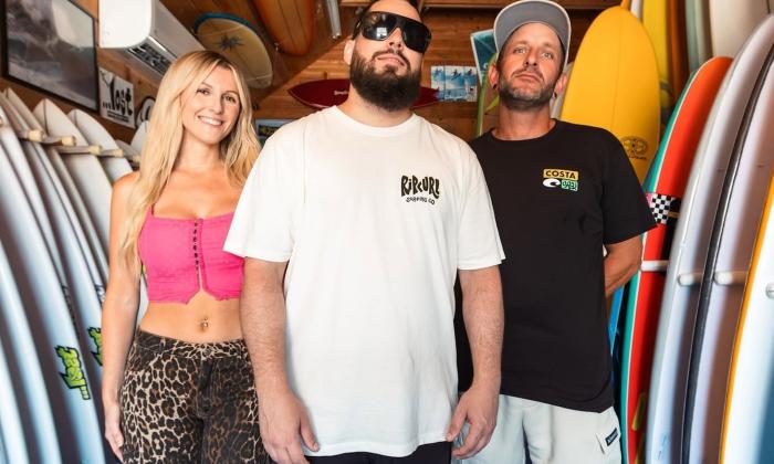 Bandmates from Seranation smile and pose next to surfboards.