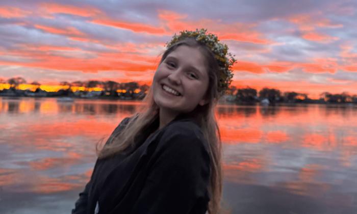 The artist bliss, wearing a flower wreath in front of an ocean sunset