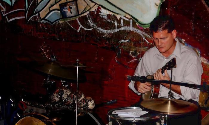 Darren Ronan playing the ukulele while sitting at the drums