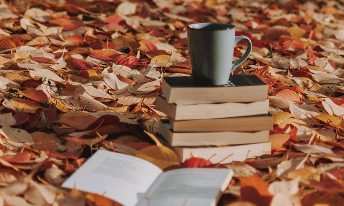 Books and a coffee cup in the middle of fall leaves