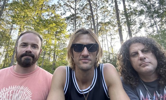 Three men, in a copse of trees, staring at the camera