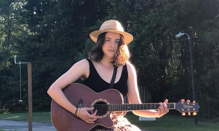 Songwriter Alivia Hunter, in a hat, with her guitar, outsite