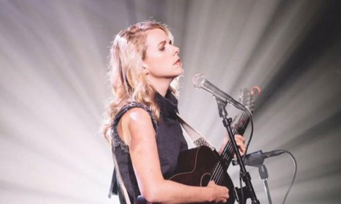 songwriter Aiofe O'Donovan singing, with guitar behind mic, sunburst motif in background