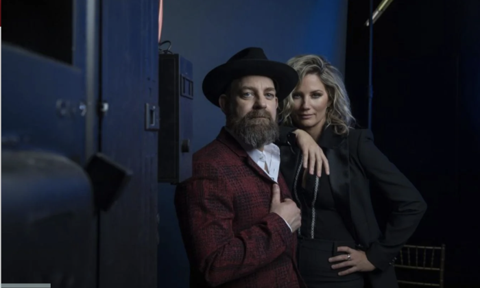 Bandmates from Sugarland huddle together and pose in front of a dark blue backdrop.
