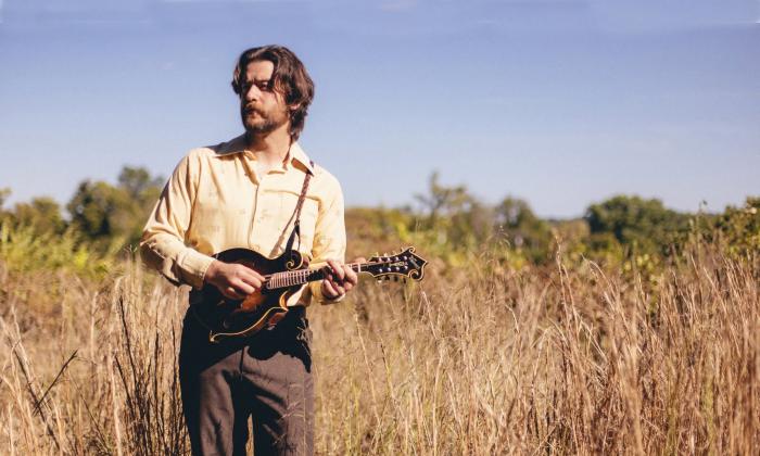 Jerrod Walker playing his mandolin while standing in a field