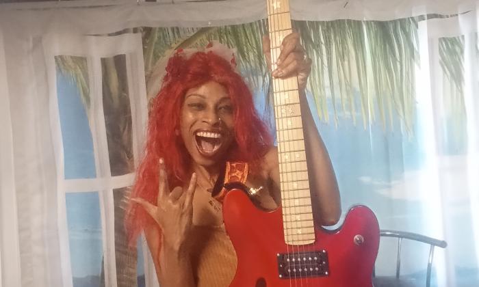 Lydia Flowers against a curtained wall, holding an electric guitar