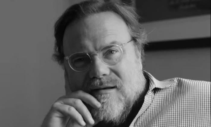Kevin Farley, wearing glasses, poses for fans with both hands cupping his cheeks. 
