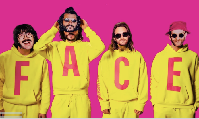 Bandmates from Goose wear yellow clothing and pose in front of a pink backdrop.