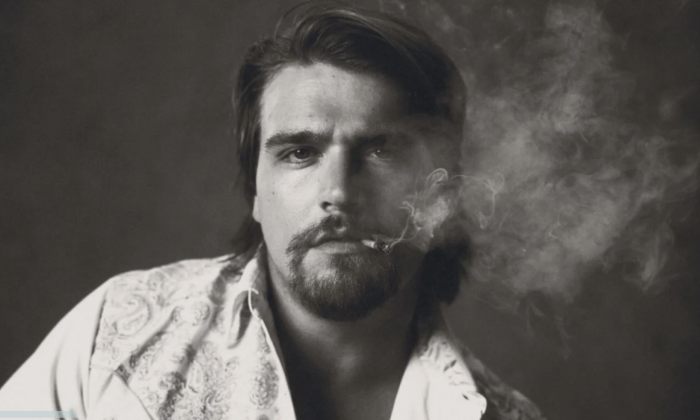 Gavin Adcock smokes a cigarette and poses in front of a grey backdrop.