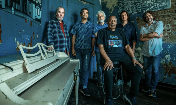 Little Feat huddle together and pose in front of a dark blue backdrop.