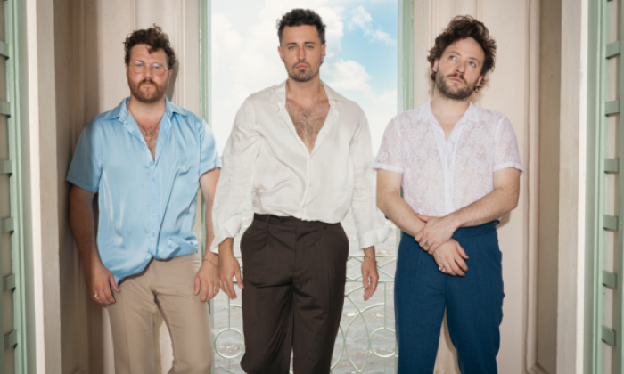 Bandmates from Raynes pose in front of a window with curtains.