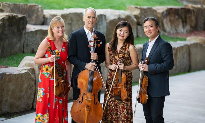 The four members of a string quartet, standing outside and holding their instruments
