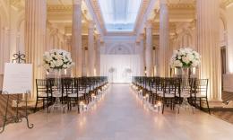 Before the wedding, chairs, flowers, and candles are waiting for guests to arrive, in a room with white columns
