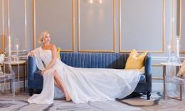 A bride in a contempory one-shoulder white gown, relaxes on a blue sofa