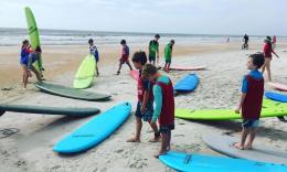Students at Stoked to Surf Camp spread on the sand with blue and lime-green surf boards