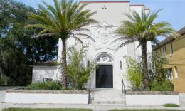 Front of the white synagogue from Cordova street, with palm trees and rosemary bushes on either side of the stairs leading to the front door.