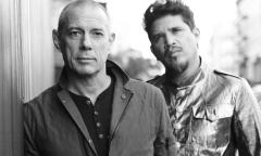 Members of Thievery Corporation stand beside a wall.