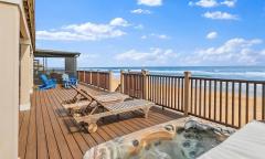 A stunning back deck with lounge chairs and a hot tub overlooking the ocean