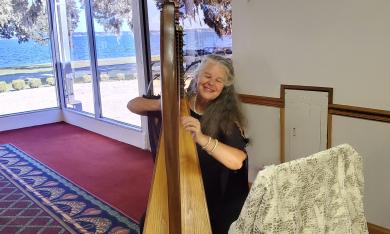 De Luna, Harpist, performing in a venue near the water, in a room with beige walls and burgundy carpeting.