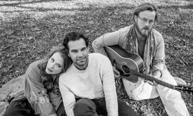 Members of the Lone Bellow Trio sitting on a lawn, one with a guitar