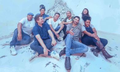 Members of the Cat Empire smile and pose in front of a blue background.