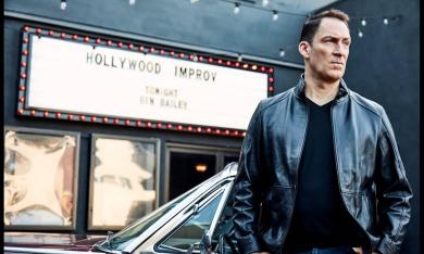 Ben Bailey poses in front of a car and a theater. 
