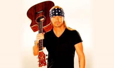 Bret Michaels holds his guitar upside down in front of a white background. 