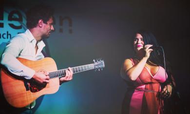 Alberto Cebollero with a guitar and Ramona at the microphone, performing on stage