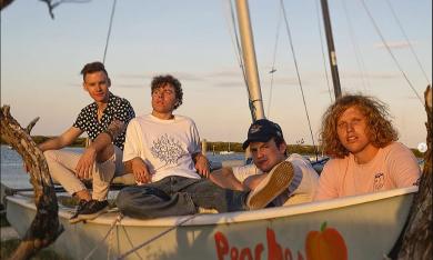 The four members of King Peach sitting in a small sailboat on land at sunset