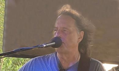 Singer songwriter David Watt Besley, with microphone, singing onstage, outside