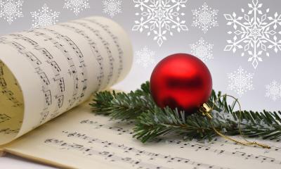 A sheet of music with a red Christmas ball decoration placed on top of it. 