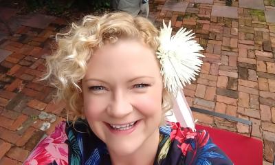 Amy Hendrickson with a flower in her hair, looking up into a camera while standing on an old brick patio